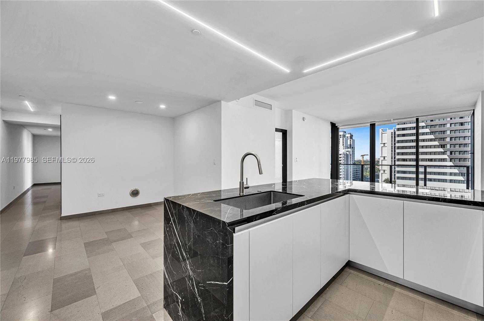 A modern kitchen features a black marble waterfall island and white cabinets against tile flooring — 88 SW 7th St # 806, Miami FL 33130, MIAMI, FL