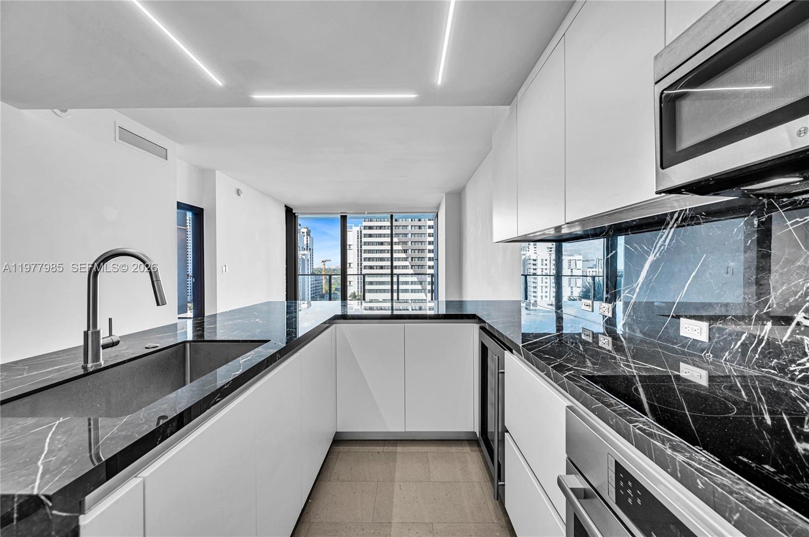 A modern kitchen features white cabinets, black marble countertops, and a view of city buildings — 88 SW 7th St # 806, Miami FL 33130, MIAMI, FL