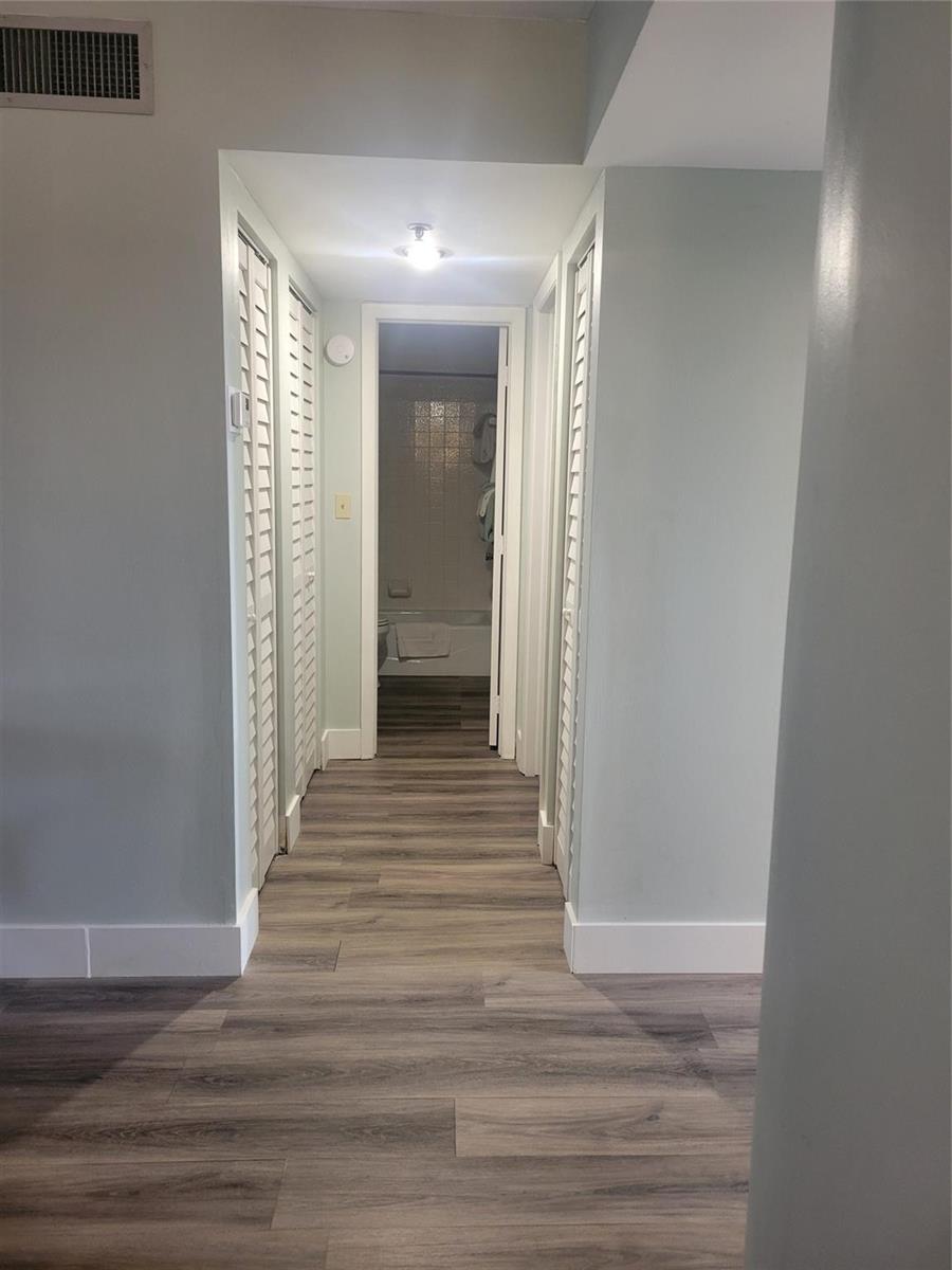 A hallway with light-colored walls, wood-look flooring, and white louvered closet doors leads to a bathroom — 3940 Inverrary Boulevard # a, Lauderhill FL 33319, LAUDERHILL, FL