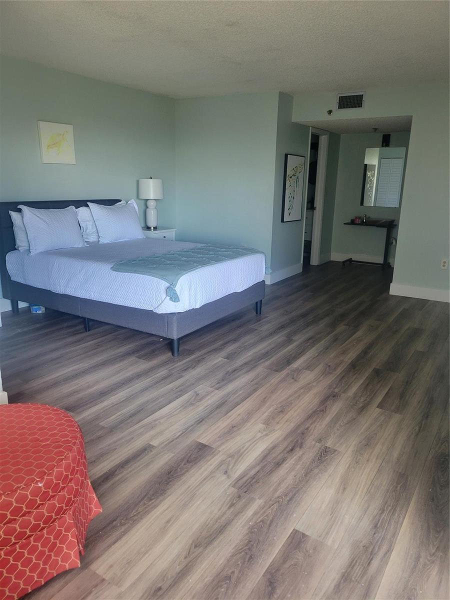 A bedroom features light green walls, wood-look flooring, and a gray upholstered bed frame — 3940 Inverrary Boulevard # a, Lauderhill FL 33319, LAUDERHILL, FL