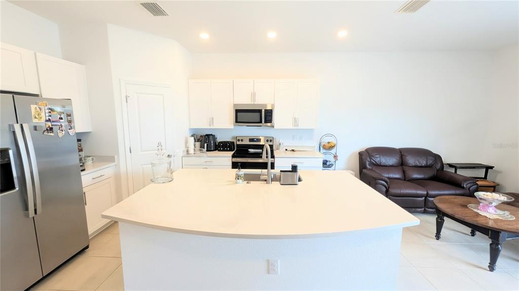 A kitchen with a center island and white cabinets opens to a living area — 5686 ARCHIPELAGO STREET, NOKOMIS, FL