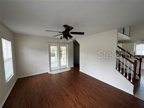 An empty living room features wood-look flooring, a ceiling fan, and a staircase with railings — 130 N BOSTON AVENUE, DELAND, FL