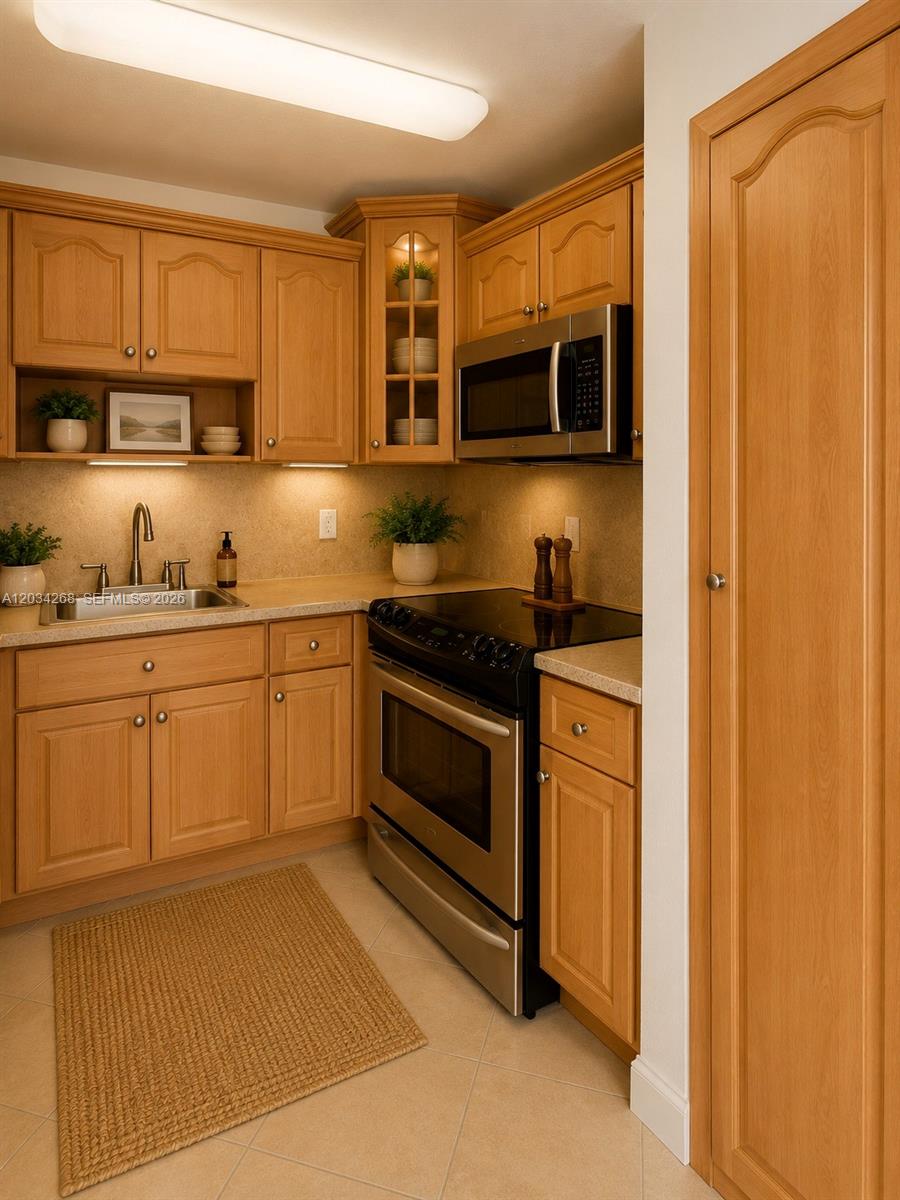 A kitchen features light wood cabinets, stainless steel appliances, and a beige tiled floor — 3041 W 76th St # 108, Hialeah FL 33018, HIALEAH, FL