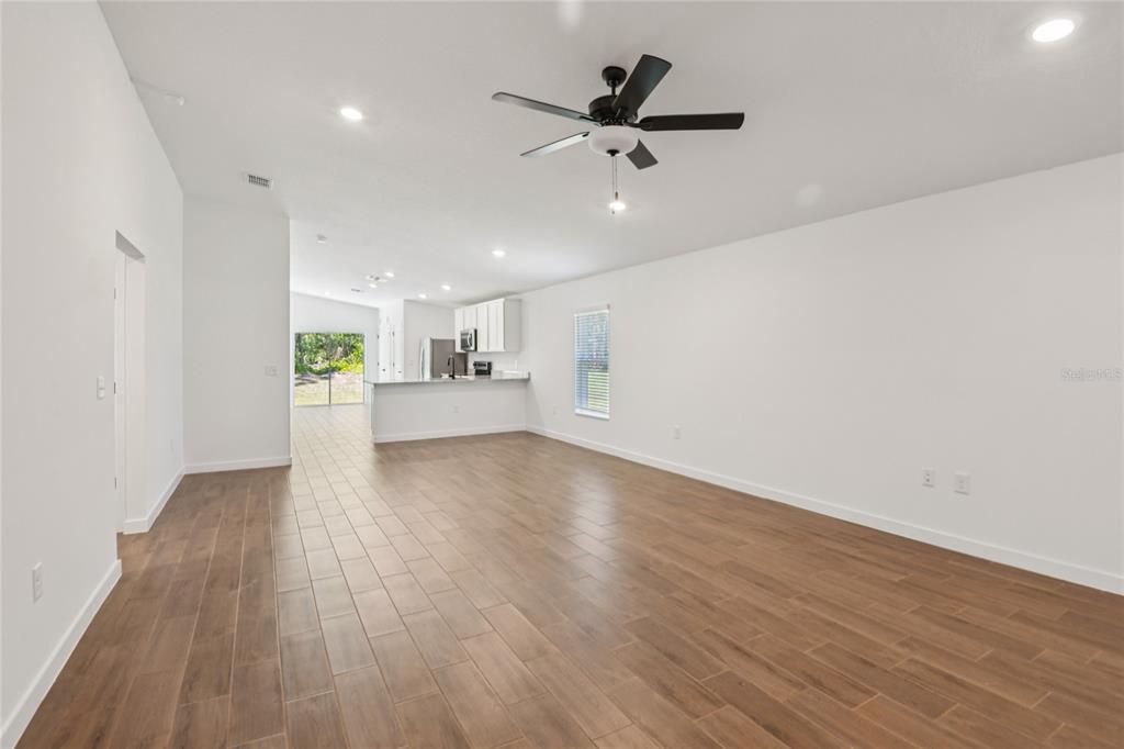 A bright, open-concept living area features wood-look tile flooring, white walls, and a ceiling fan — 14034 RICEBIRD AVENUE, WEEKI WACHEE, FL