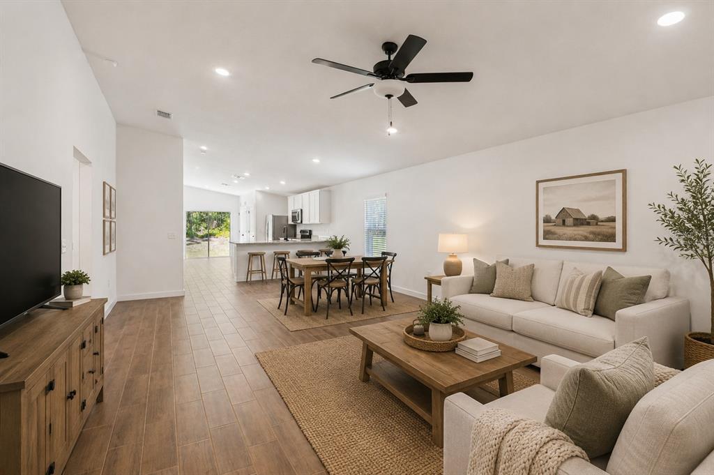 An open-concept living and dining area features wood-look tile floors, white walls, and neutral furniture — 14034 RICEBIRD AVENUE, WEEKI WACHEE, FL
