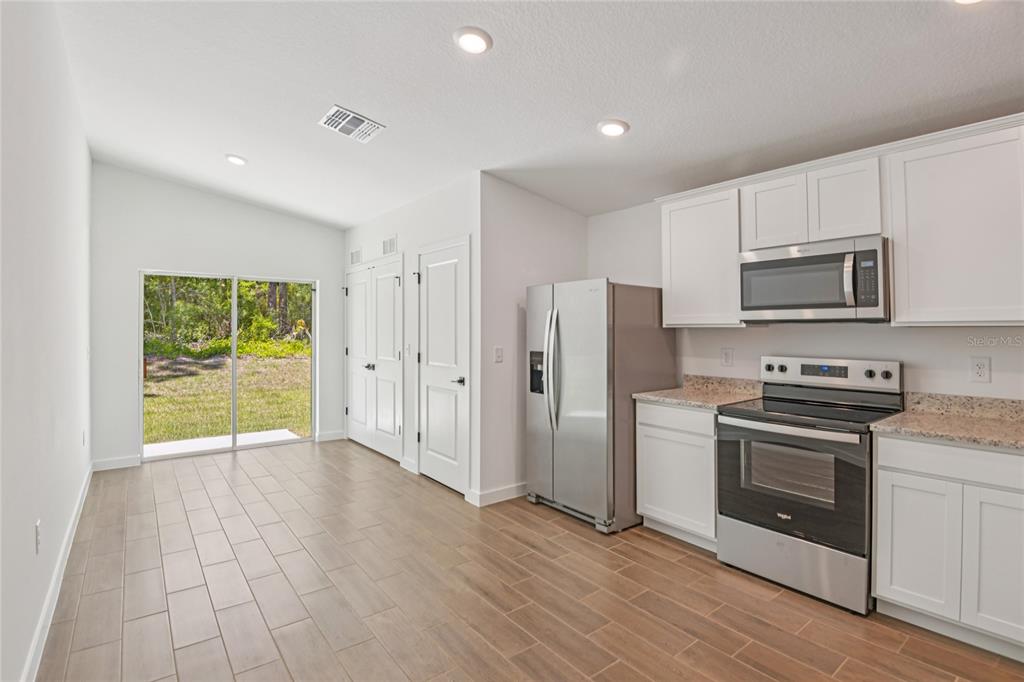 A kitchen with white cabinets, stainless steel appliances, and tile flooring next to a sliding door — 14034 RICEBIRD AVENUE, WEEKI WACHEE, FL