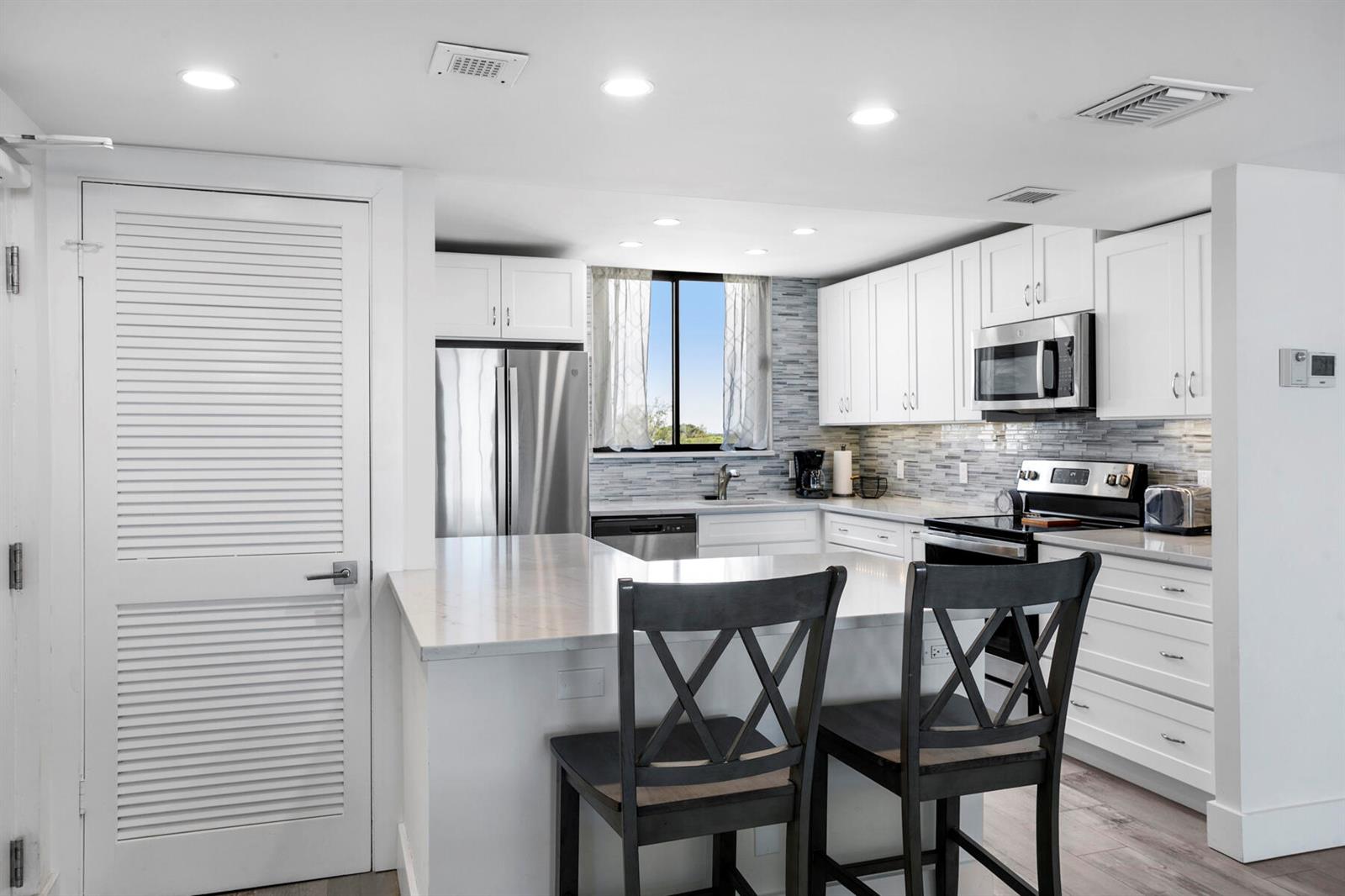 A kitchen with white cabinets, stainless steel appliances, a quartz island, and two wooden chairs — 300 Ocean Trail Way # 510, Jupiter FL 33477, JUPITER, FL