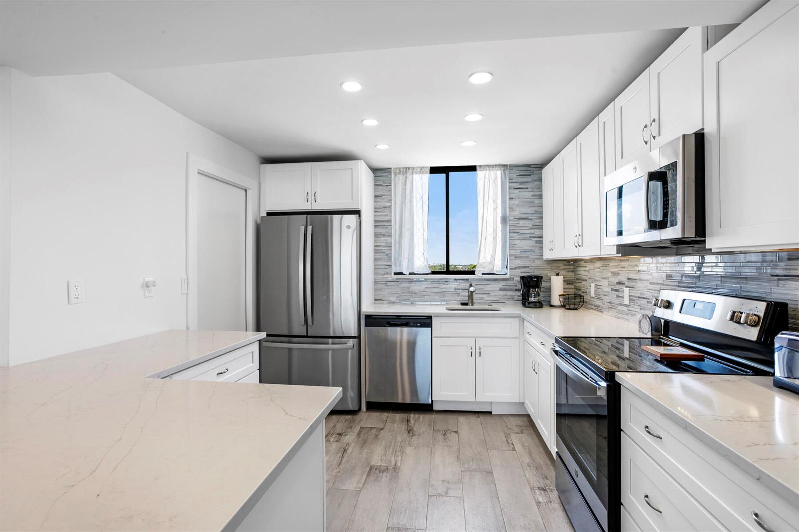 A modern kitchen features white cabinets, stainless steel appliances, quartz countertops, and wood-look tile flooring — 300 Ocean Trail Way # 510, Jupiter FL 33477, JUPITER, FL