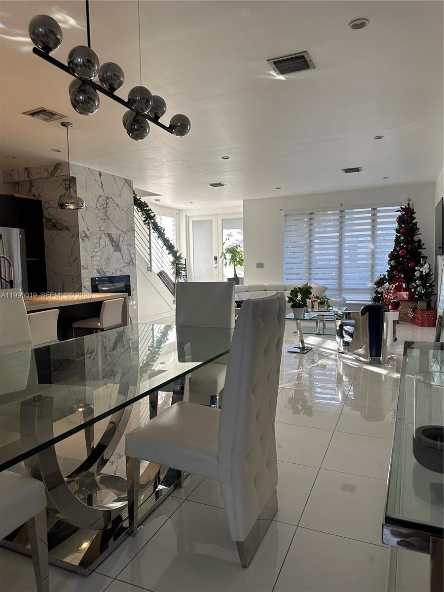 A modern dining area features a glass table, white tufted chairs, and a statement chandelier — 10361 NW 64th Ter, Doral FL 33178, DORAL, FL