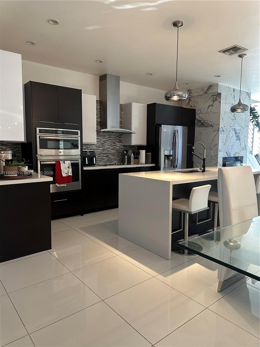 A modern kitchen features dark cabinetry, a white waterfall island, and stainless steel appliances — 10361 NW 64th Ter, Doral FL 33178, DORAL, FL