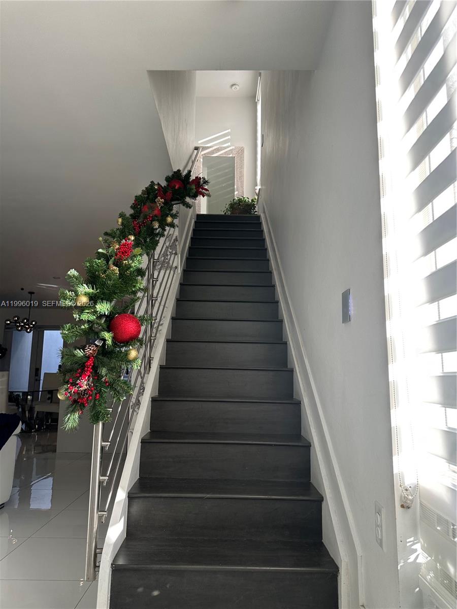 A staircase with dark wood treads and a festive garland railing leads to an upper landing — 10361 NW 64th Ter, Doral FL 33178, DORAL, FL