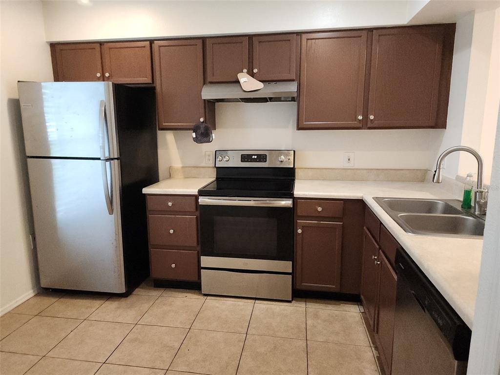 A kitchen with brown cabinets, stainless steel appliances, white countertops, and tiled flooring — 13336 FAIRWAY GLEN DRIVE UNIT 104, ORLANDO, FL