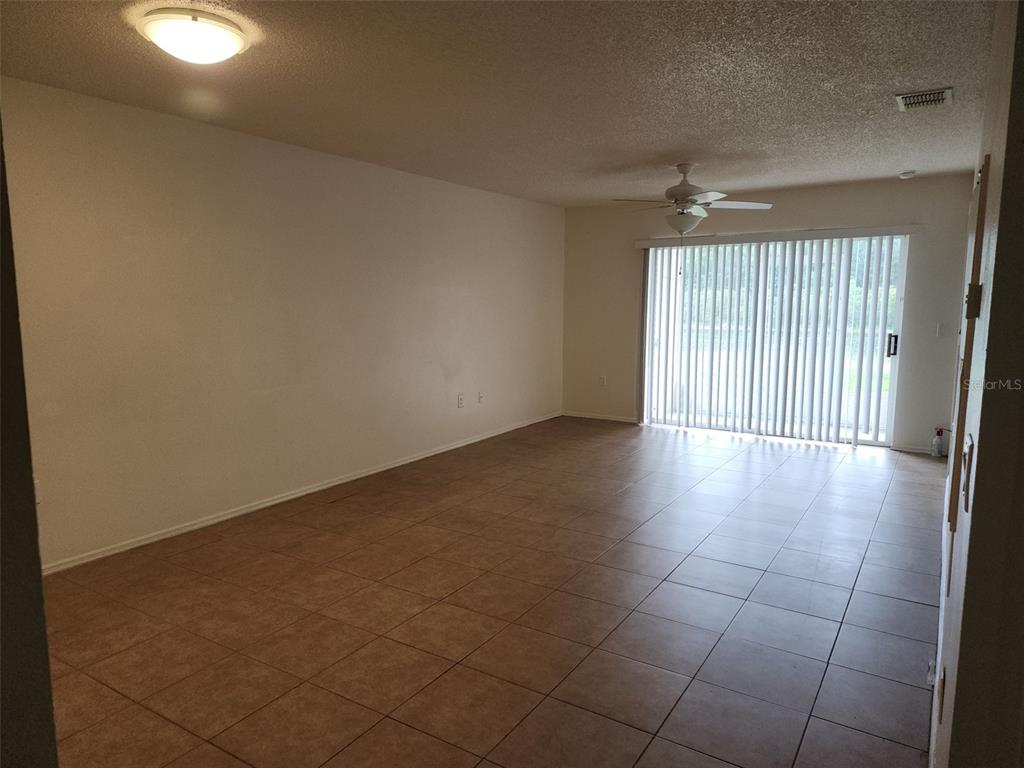 An empty living room features beige tile flooring, a ceiling fan, and sliding glass doors — 13336 FAIRWAY GLEN DRIVE UNIT 104, ORLANDO, FL