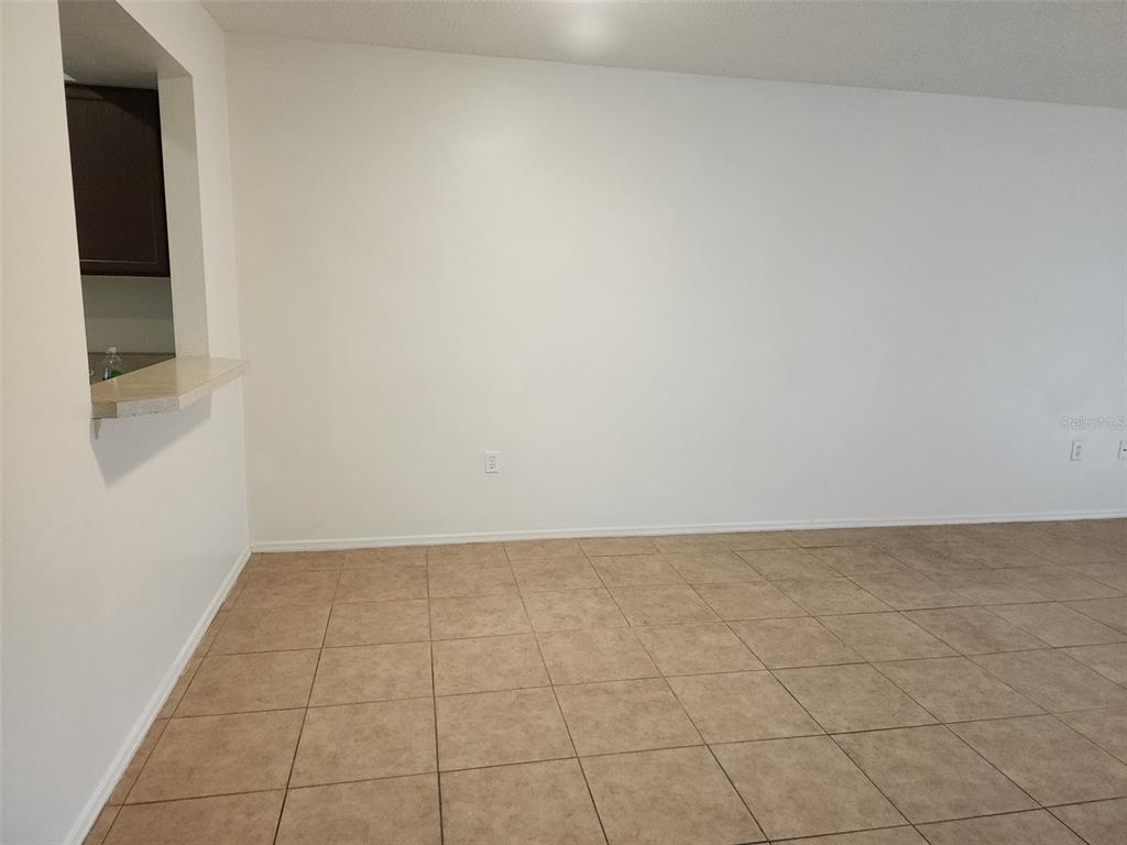 An empty room with beige tile flooring, white walls, and a kitchen pass-through window — 13336 FAIRWAY GLEN DRIVE UNIT 104, ORLANDO, FL