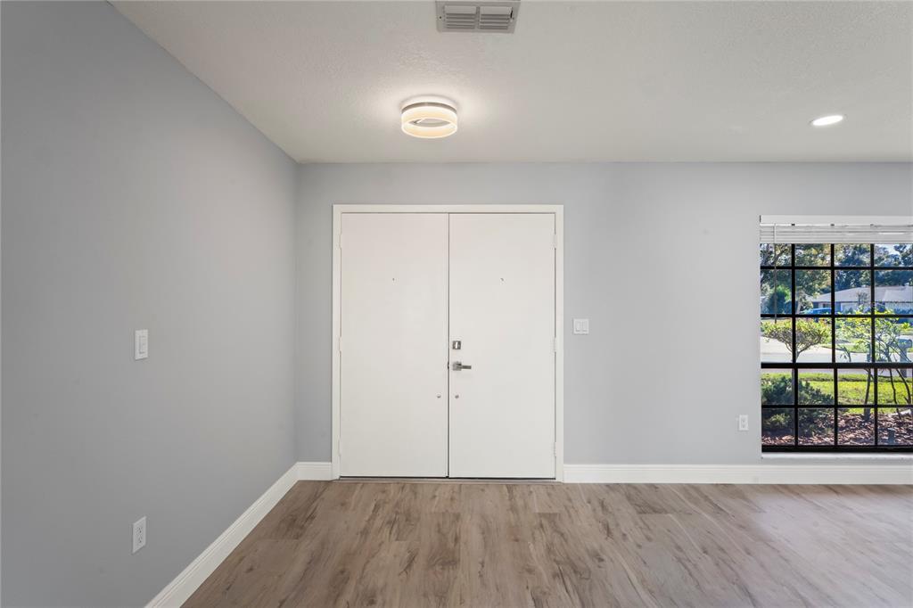 An empty room with light gray walls, wood-look flooring, double entry doors, and a window — 8312 ROXBORO DRIVE, HUDSON, FL