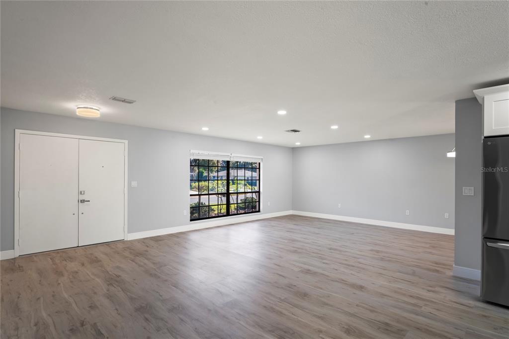 A spacious, light-gray living room features wood-look flooring, a large window, and recessed lighting — 8312 ROXBORO DRIVE, HUDSON, FL