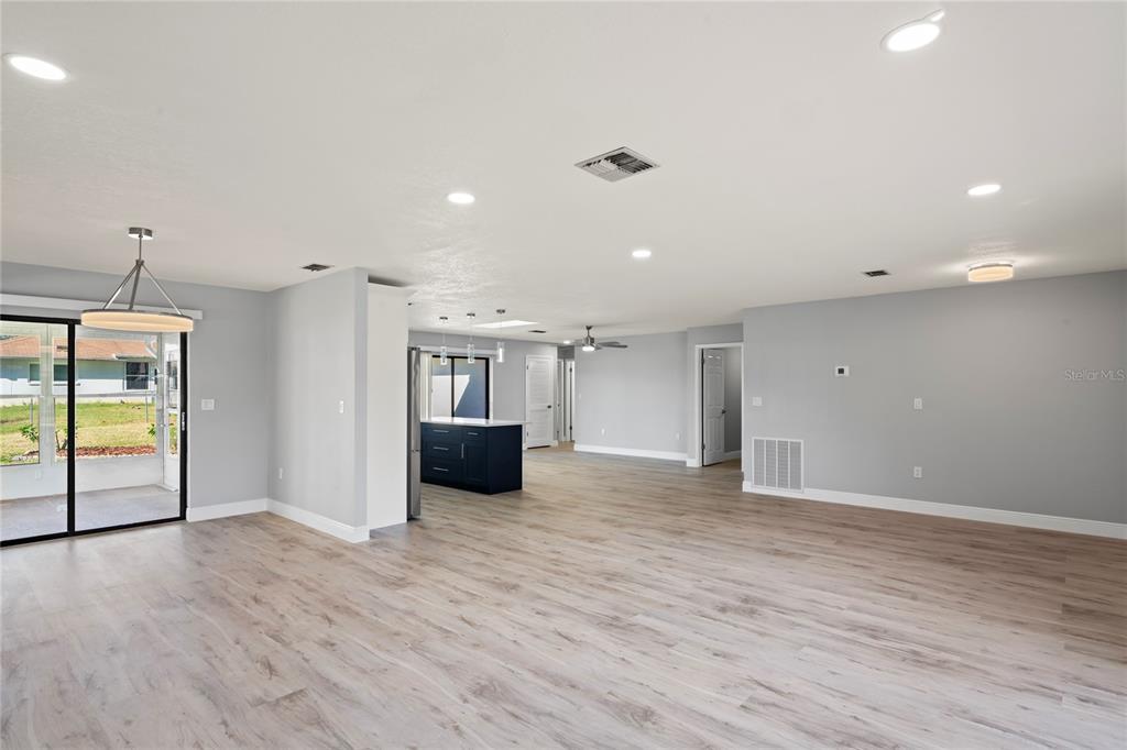 An open-concept living area features light wood-look flooring, gray walls, and a dark kitchen island — 8312 ROXBORO DRIVE, HUDSON, FL