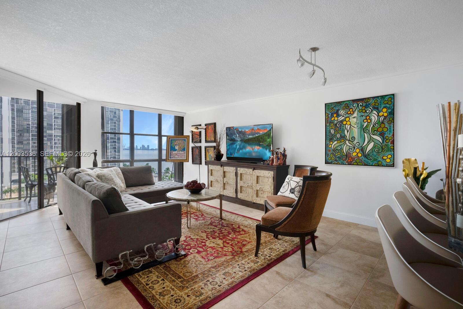 A living room features a grey sectional, a patterned rug, and floor-to-ceiling windows with views — 1925 Brickell Ave # 1003, Miami FL 33129, MIAMI, FL