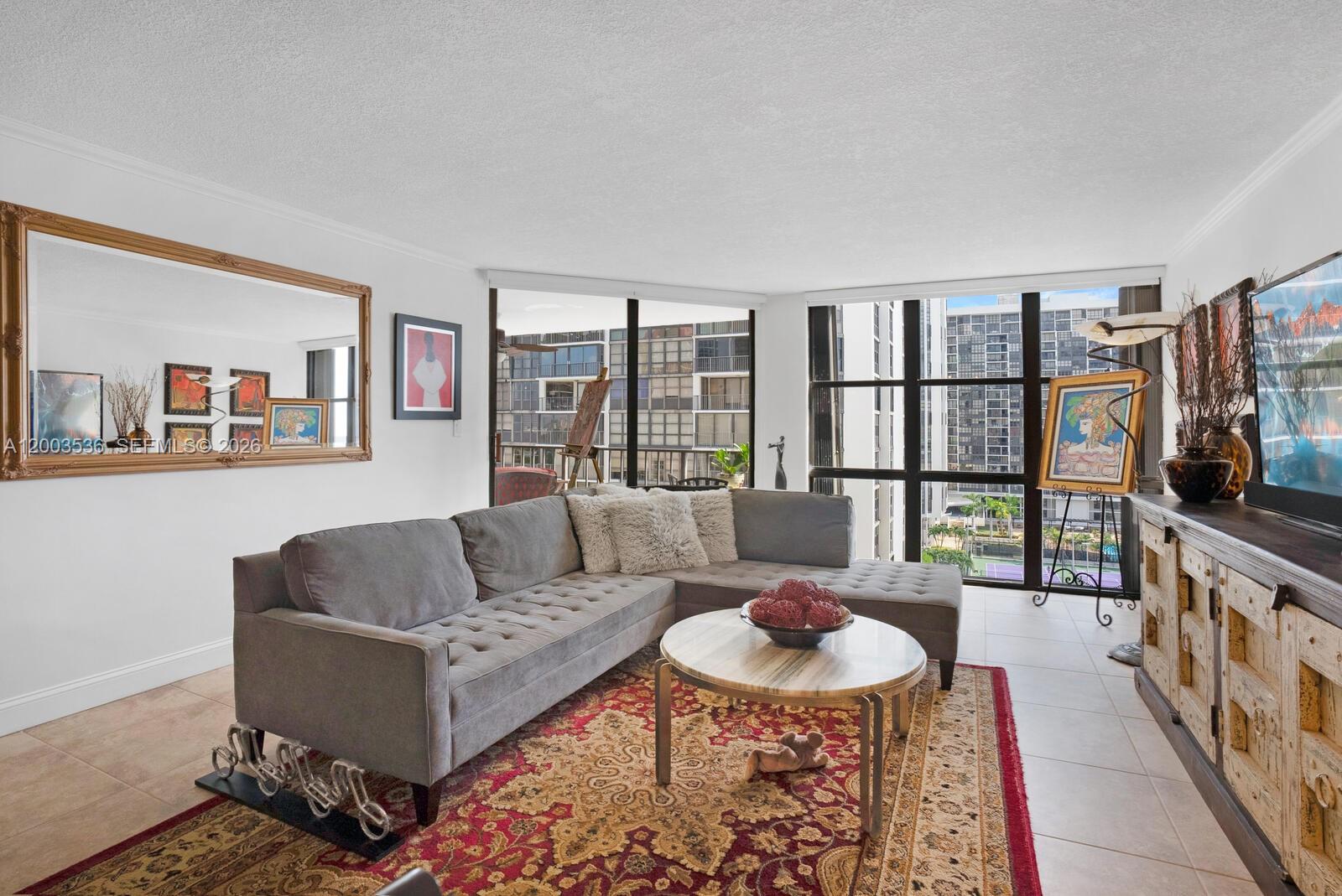 A living room features a gray sectional sofa, a patterned rug, and floor-to-ceiling windows — 1925 Brickell Ave # 1003, Miami FL 33129, MIAMI, FL