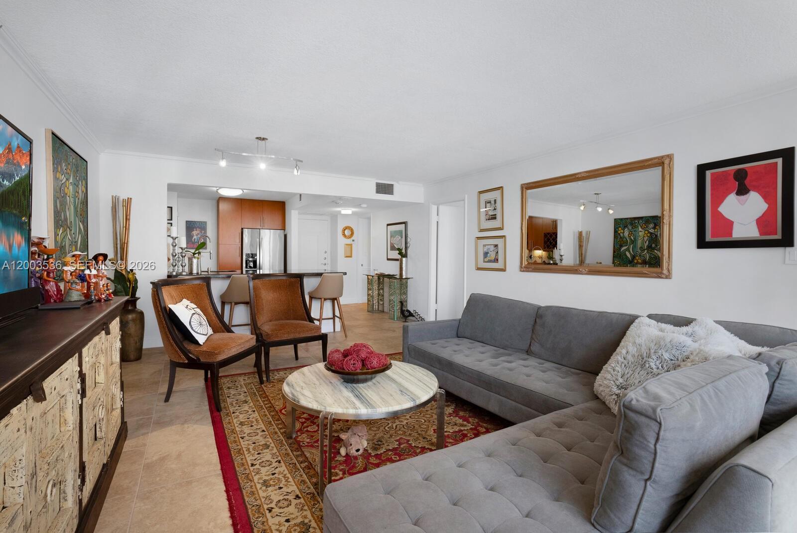 A living room features a grey sectional sofa, two brown chairs, and a round coffee table — 1925 Brickell Ave # 1003, Miami FL 33129, MIAMI, FL