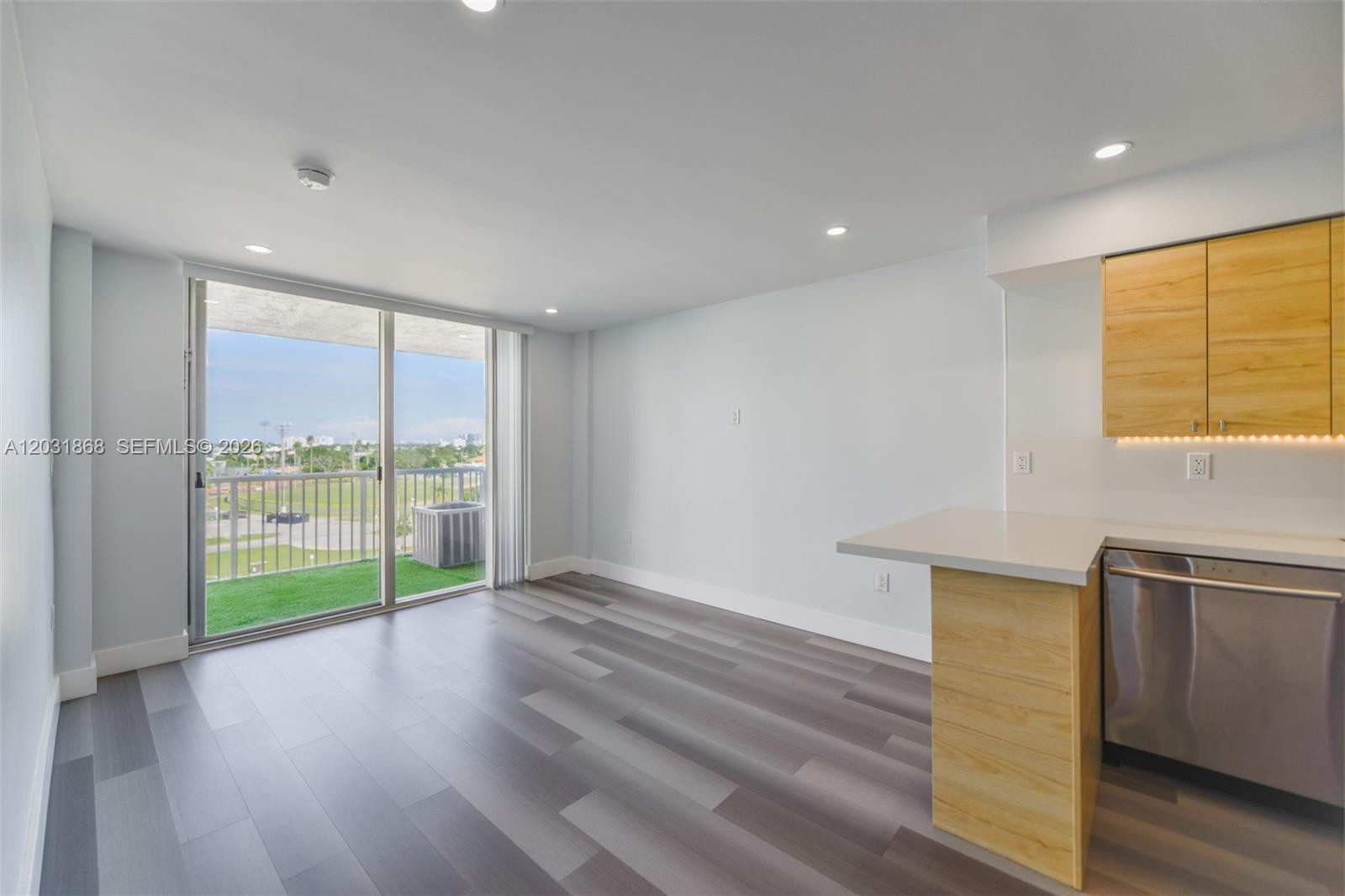 An open-plan living area features wood-look flooring, light-colored walls, a kitchen peninsula, and a balcony — 1800 NW 24th Ave # 712, Miami FL 33125, MIAMI, FL