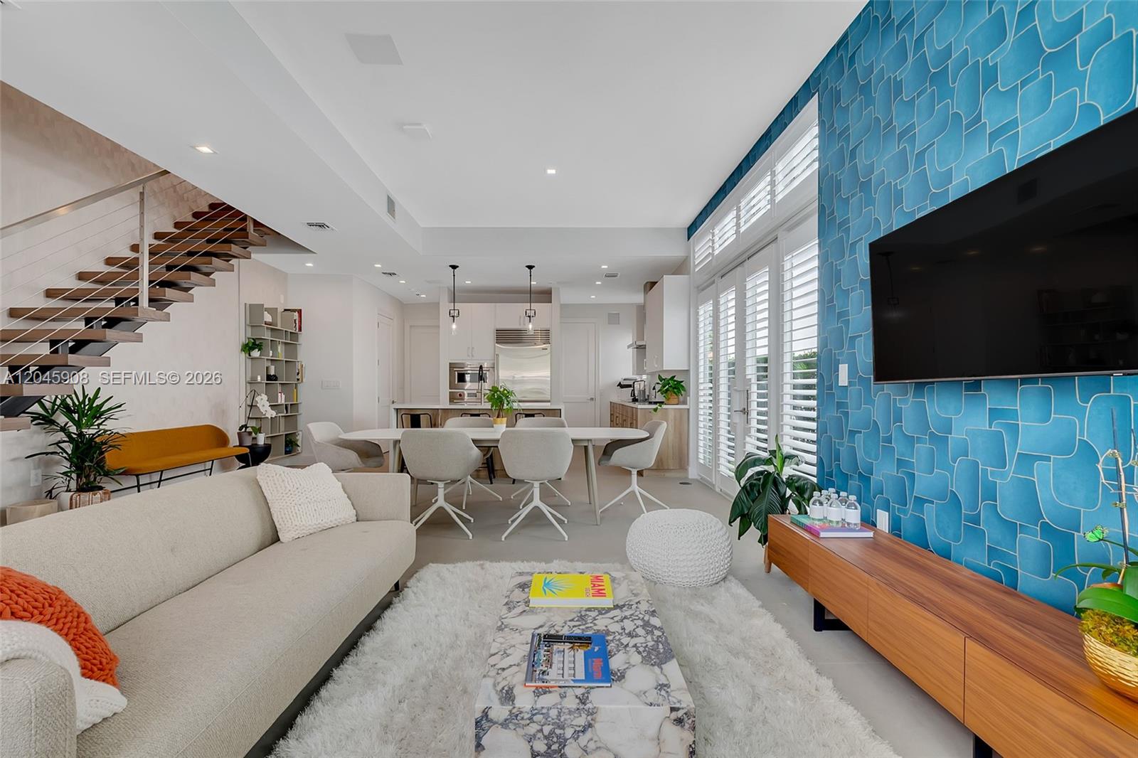 A modern open-concept living and dining area features a blue patterned accent wall and staircase — 3406 Ponce De Leon Blvd, Coral Gables FL 33134, CORAL GABLES, FL