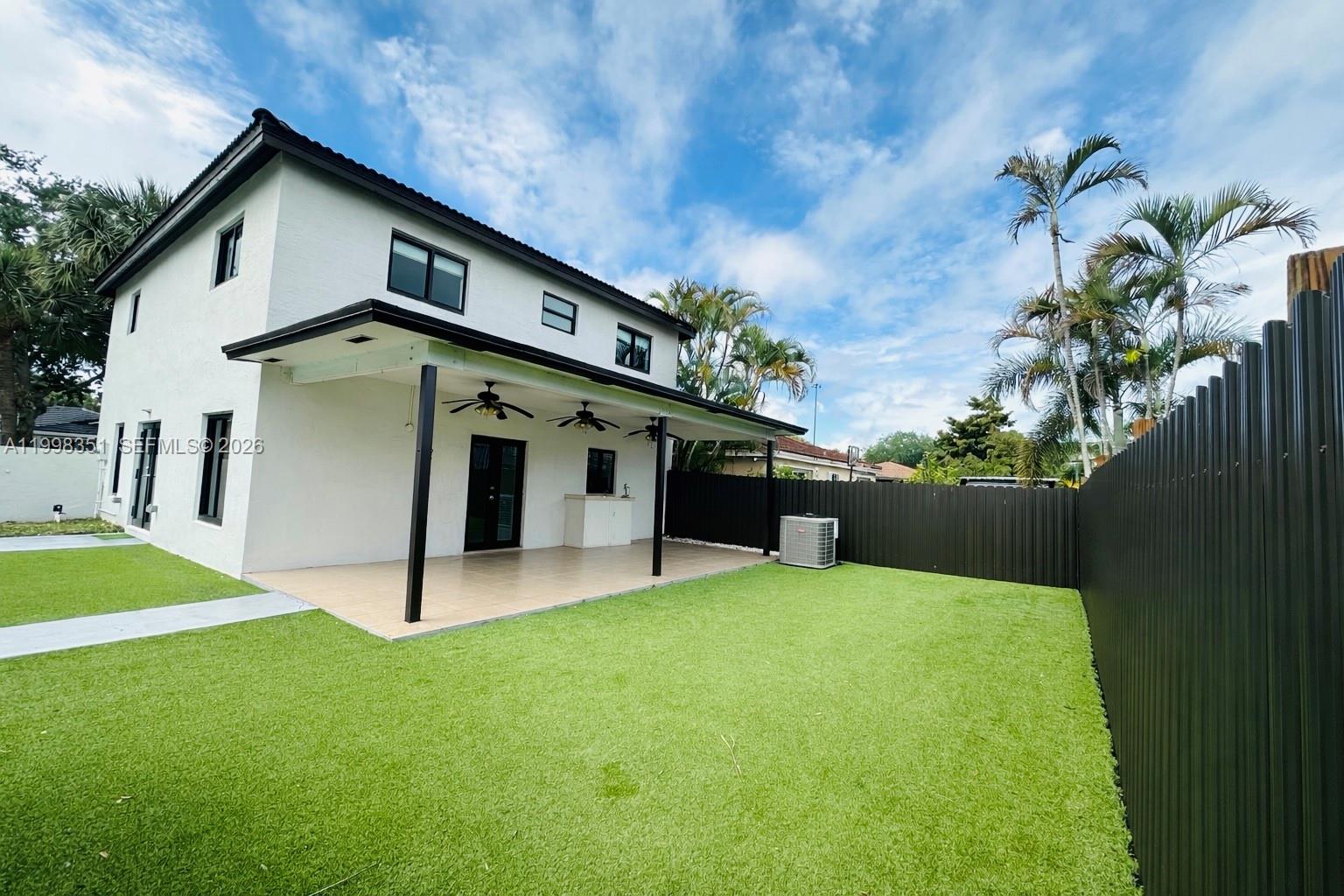 A two-story white house features a covered patio, artificial turf lawn, and dark metal fencing — 9069 NW 193rd St, Hialeah FL 33018, HIALEAH, FL