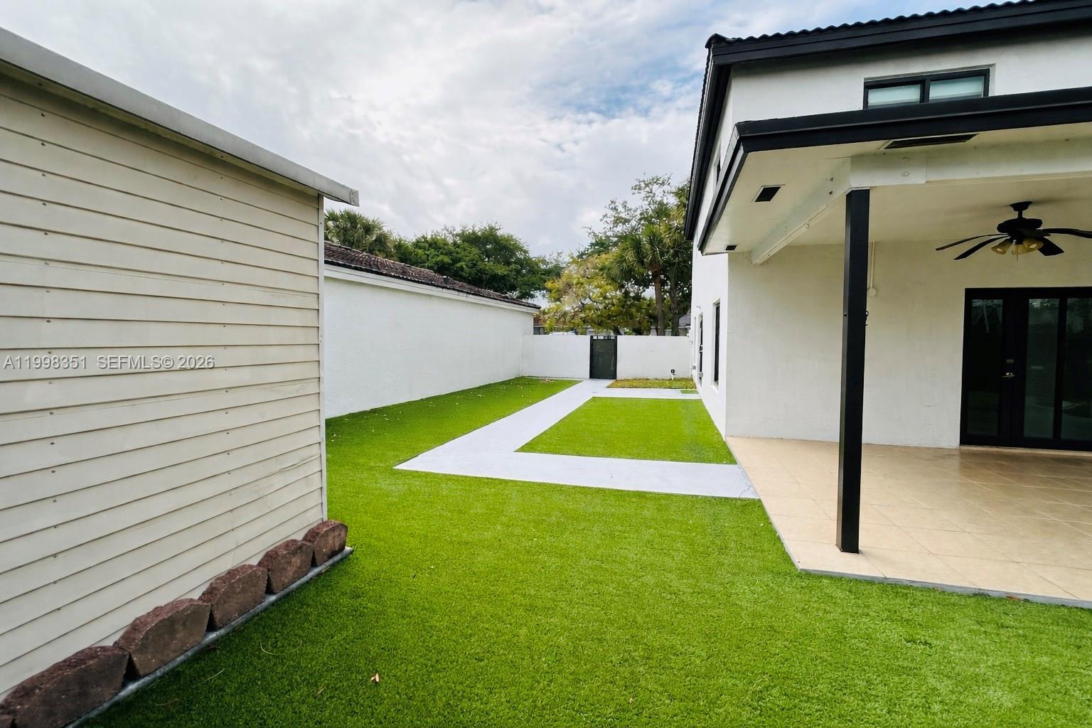 A backyard features artificial turf, a concrete walkway, and a covered patio area — 9069 NW 193rd St, Hialeah FL 33018, HIALEAH, FL