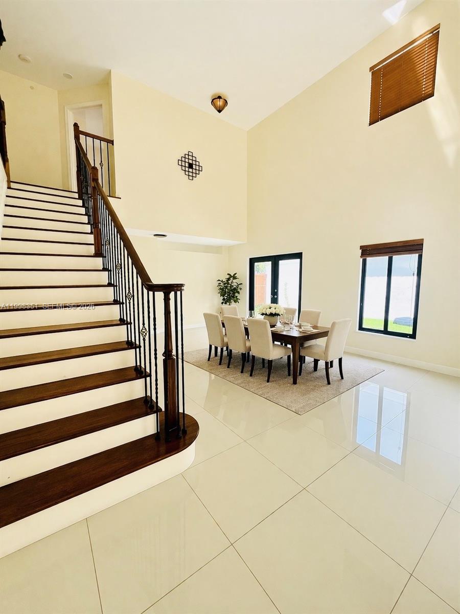 A dining area with a wooden table and chairs sits beneath a high-ceilinged staircase — 9069 NW 193rd St, Hialeah FL 33018, HIALEAH, FL