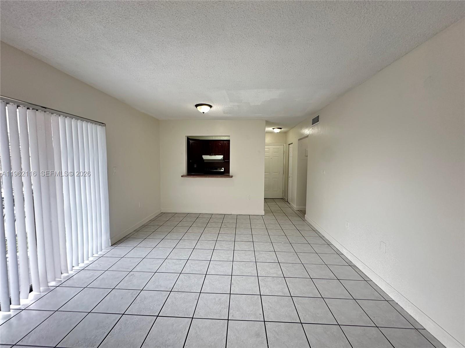 An empty room features white walls, light-colored tile flooring, and a kitchen pass-through window — 1008 NW 45th Ave # 9, Miami FL 33126, MIAMI, FL