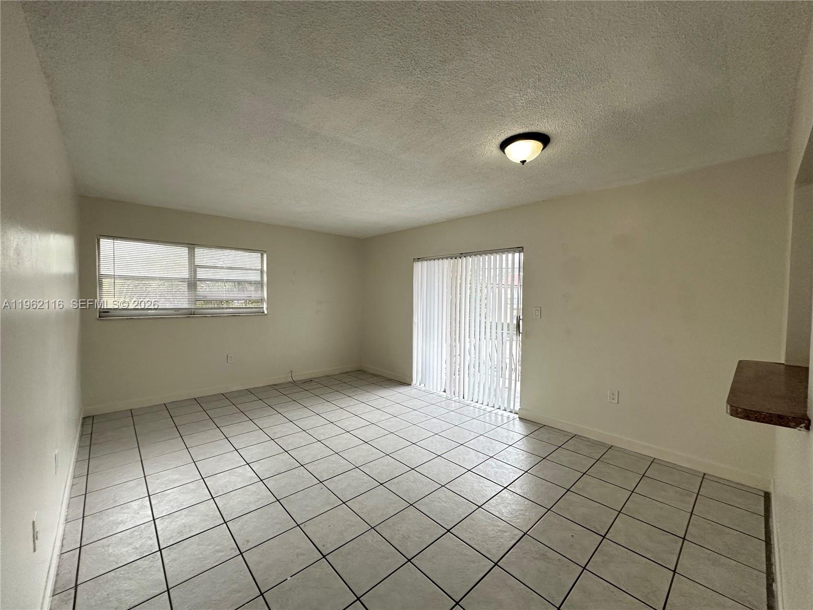 An empty room features white walls, a tiled floor, a window, and a sliding glass door — 1008 NW 45th Ave # 9, Miami FL 33126, MIAMI, FL