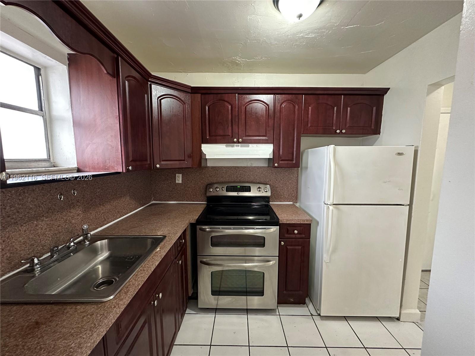 A kitchen features dark wood cabinets, speckled brown countertops, stainless steel appliances, and white tile flooring — 1008 NW 45th Ave # 9, Miami FL 33126, MIAMI, FL