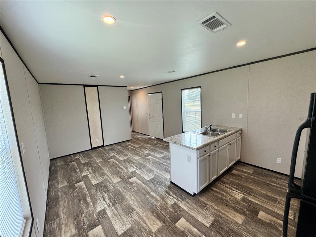 An open-concept kitchen and living area features wood-look flooring, white cabinets, and granite countertops — 1115 NW 12TH LANE, LAKE PANASOFFKEE, FL