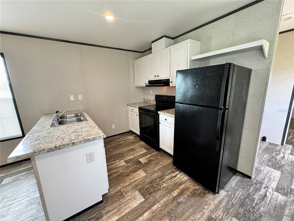 A kitchen features white cabinets, black appliances, a granite-look island, and wood-look flooring — 1115 NW 12TH LANE, LAKE PANASOFFKEE, FL