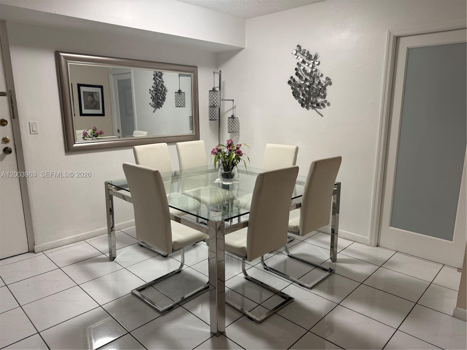A dining room features a glass-topped table with six white chairs on tiled flooring — 5033 NW 7th St # 312, Miami FL 33126, MIAMI, FL