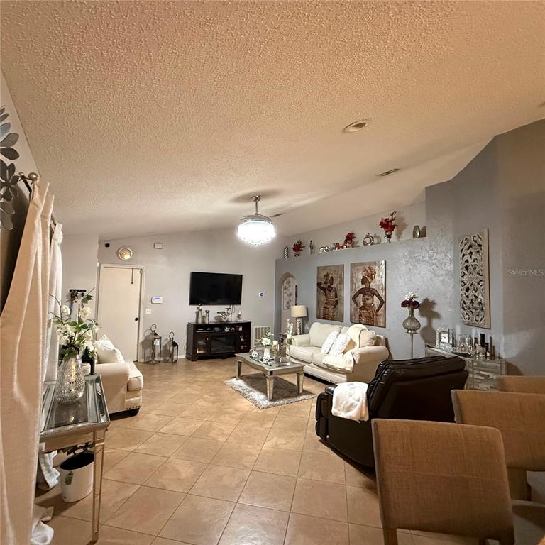 A living room features tile flooring, a vaulted ceiling, and neutral walls with decorative art — 17022 HOLMBY COURT, LAND O LAKES, FL