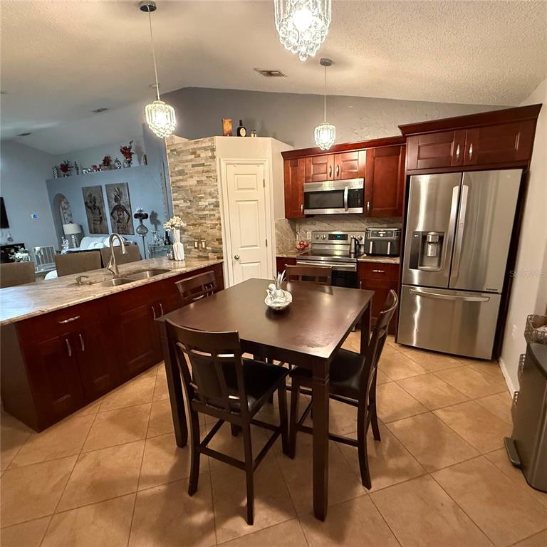 A kitchen features dark wood cabinets, stainless steel appliances, a center dining table, and tile flooring — 17022 HOLMBY COURT, LAND O LAKES, FL