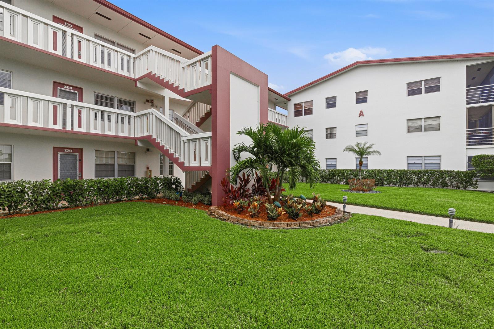 Exterior view of a multi-story apartment building with stairs, a lawn, and landscaping — 32 Fanshaw A # 32, Boca Raton FL 33434, BOCA RATON, FL
