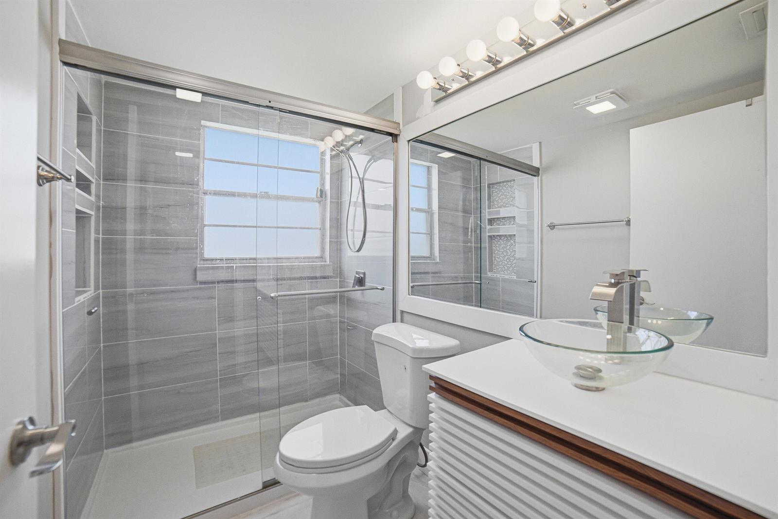 A bathroom features a glass vessel sink, a walk-in shower with gray tile, and a toilet — 32 Fanshaw A # 32, Boca Raton FL 33434, BOCA RATON, FL