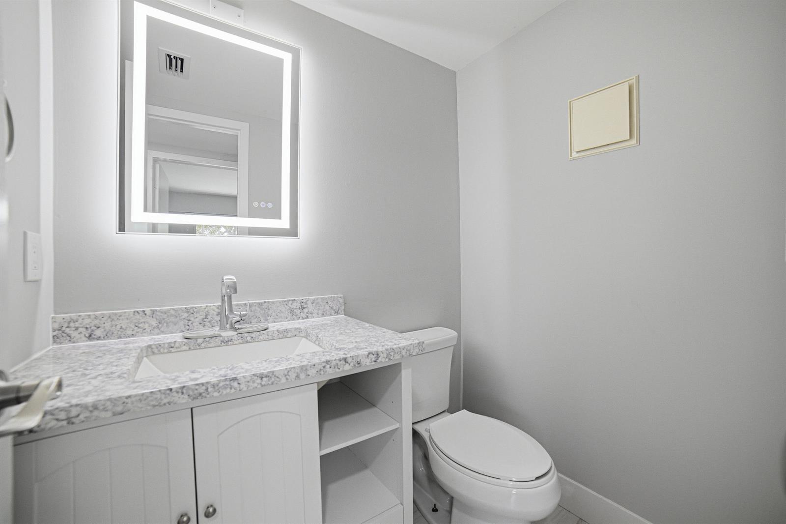 A bathroom featuring a white vanity with a speckled countertop, a toilet, and a lighted mirror — 32 Fanshaw A # 32, Boca Raton FL 33434, BOCA RATON, FL