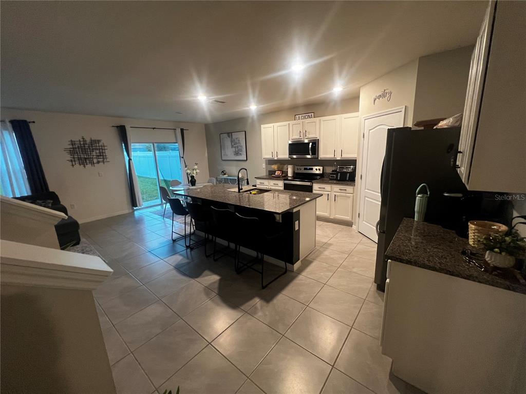 An open-concept kitchen features a granite island, white cabinetry, and tile flooring — 3906 RESTING ROBIN AVENUE, BARTOW, FL