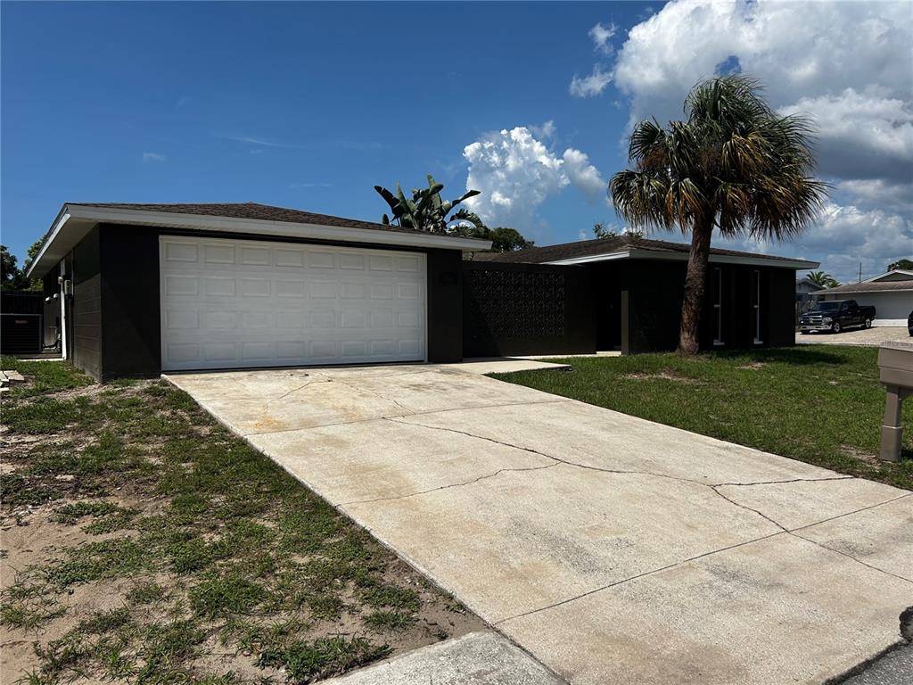 A dark-painted single-story house features a white garage door, a concrete driveway, and a palm tree — 7335 GULF HIGHLANDS DRIVE, PORT RICHEY, FL