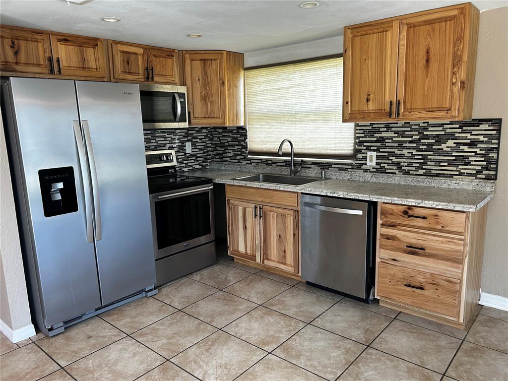 A kitchen features stainless steel appliances, wood cabinets, granite countertops, and a tiled backsplash — 7335 GULF HIGHLANDS DRIVE, PORT RICHEY, FL