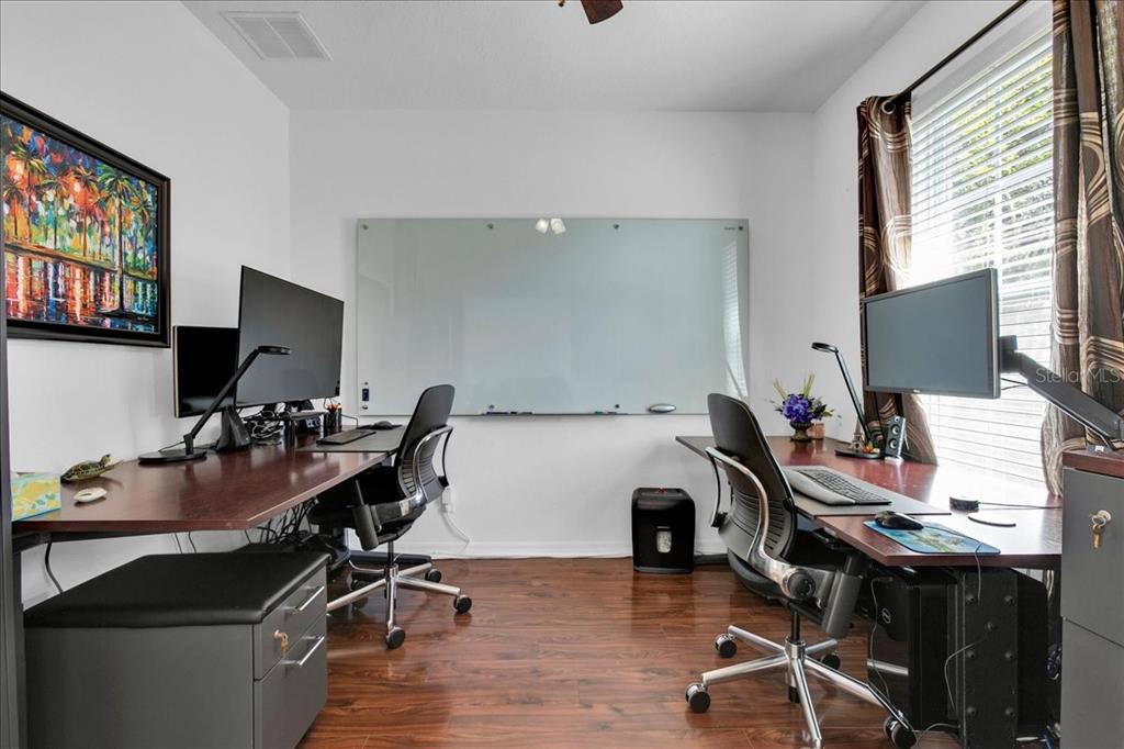 A home office features two desks with computer setups, a large glass whiteboard, and wood flooring — 9249 IVYWOOD STREET, CLERMONT, FL