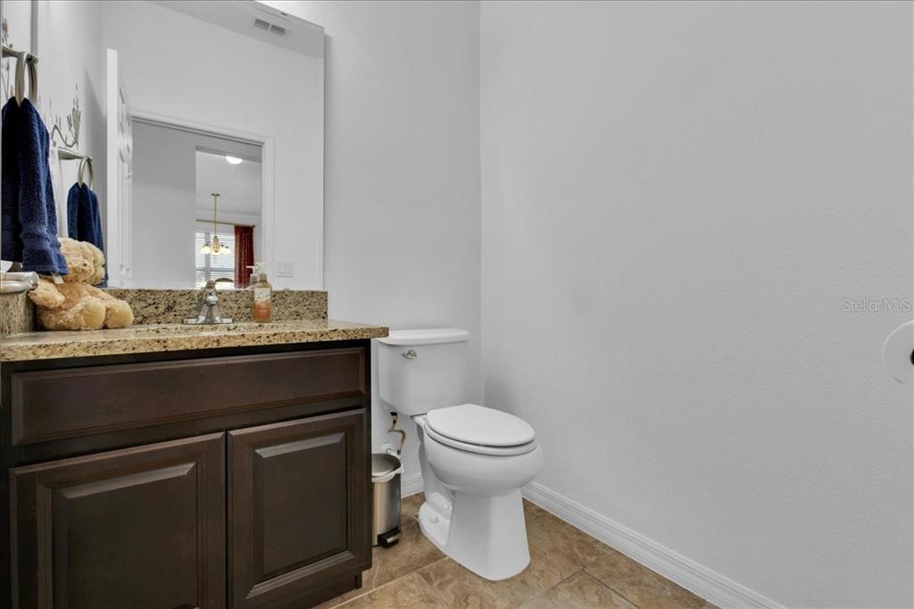 A bathroom features a granite-topped vanity with dark wood cabinets, a toilet, and tile flooring — 9249 IVYWOOD STREET, CLERMONT, FL