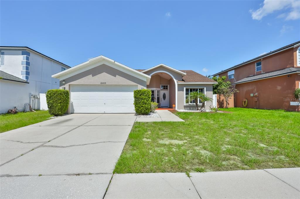 A single-story house with a white garage door, beige stucco exterior, and a front lawn — 13403 BEECHBERRY DRIVE, RIVERVIEW, FL