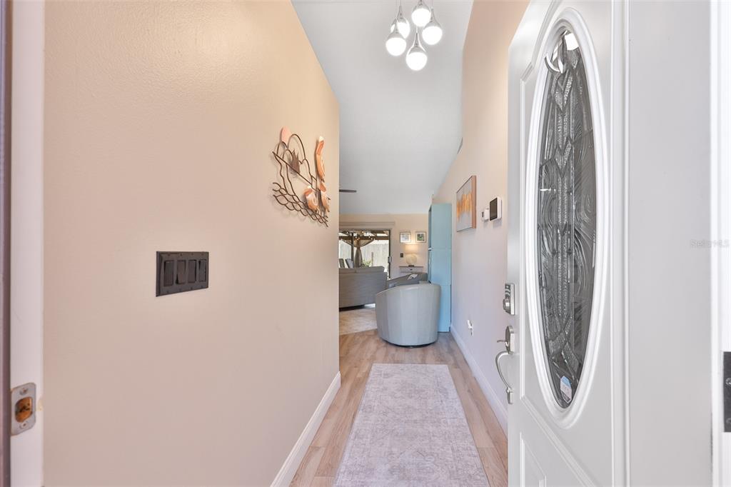 An entryway with light wood flooring leads into a living area with a vaulted ceiling — 13403 BEECHBERRY DRIVE, RIVERVIEW, FL