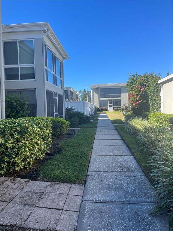 A concrete walkway leads between two-story residential buildings with screened-in porches and landscaped lawns — 689 LAKE HOWARD DRIVE NW UNIT 1E, WINTER HAVEN, FL