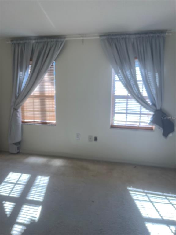 An interior room features two windows with wooden blinds and light-colored curtains over carpeted flooring — 689 LAKE HOWARD DRIVE NW UNIT 1E, WINTER HAVEN, FL
