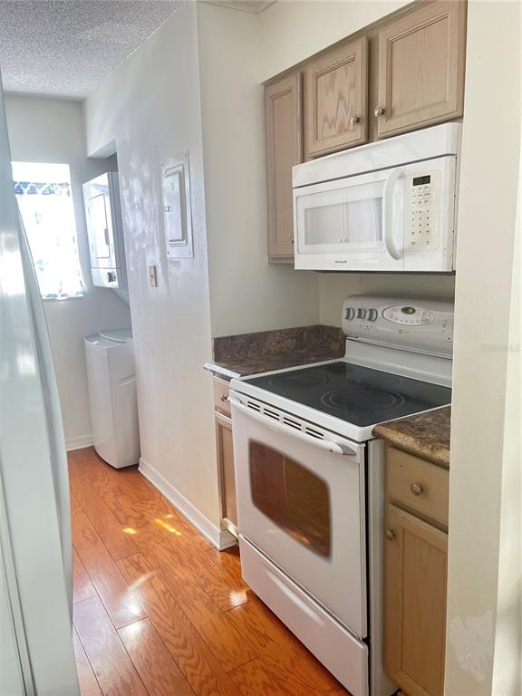 A kitchen features wood cabinets, a white stove, a microwave, and adjacent laundry appliances — 689 LAKE HOWARD DRIVE NW UNIT 1E, WINTER HAVEN, FL
